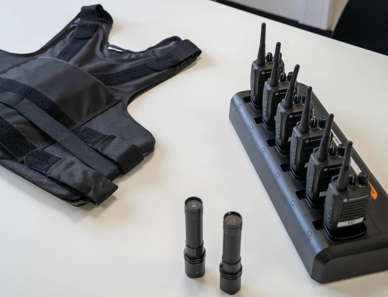Ausrüstung von security reasons: Schutzweste, Funkgeräte in der Ladeschale und zwei Taschenlampen