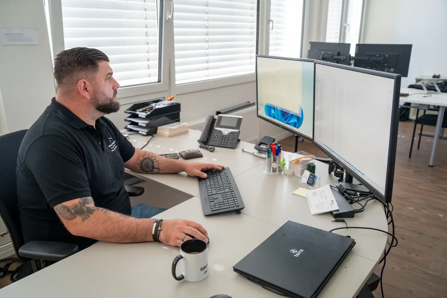 Mitarbeiter von security reasons am Arbeitsplatz mit zwei Bildschirmen und Tischtelefon