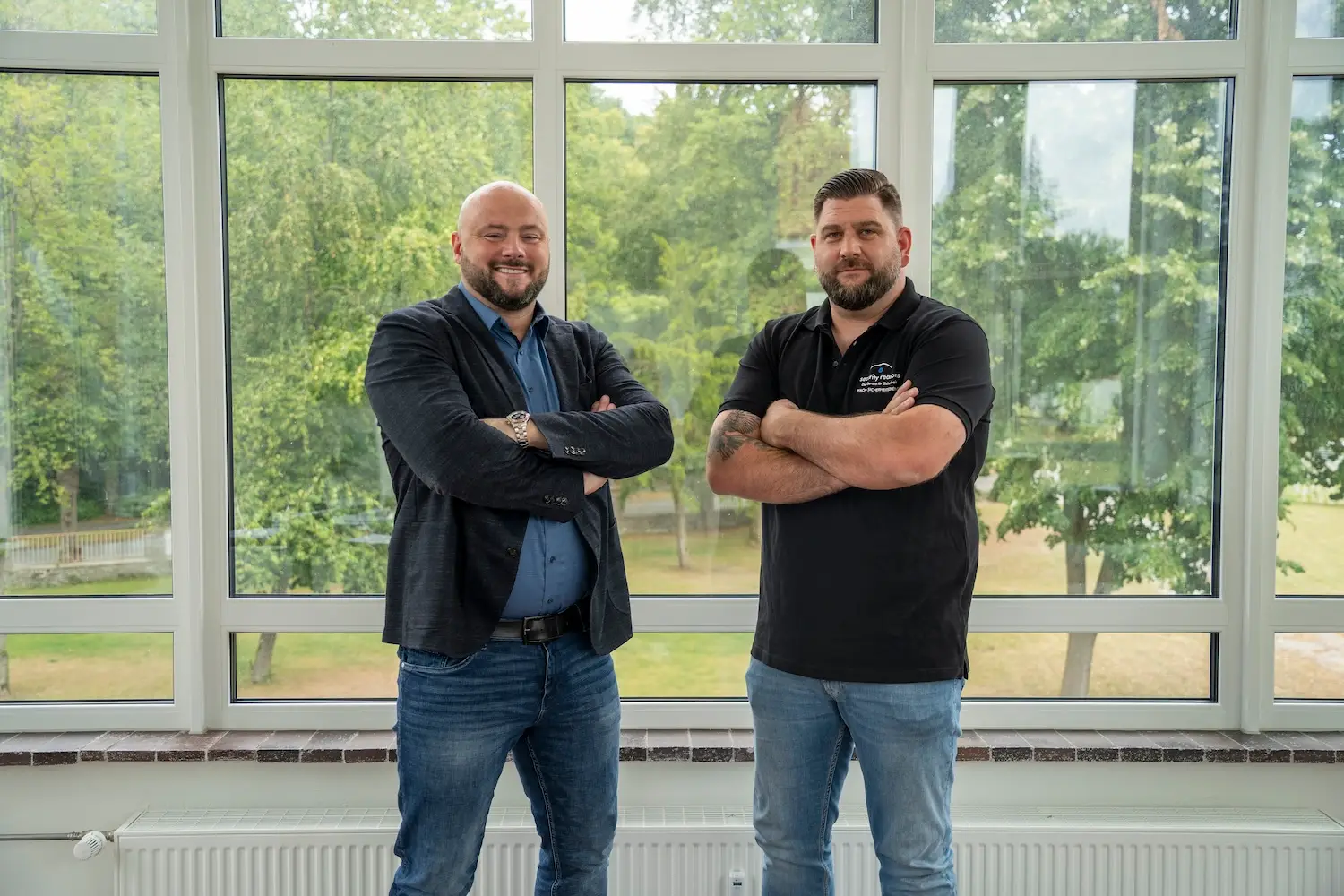 Stefan Flohr, Geschäftsführer von security reasons, und ein Mitarbeiter mit verschränkten Armen vor der Fensterfront des Büros in Bad Lippspringe