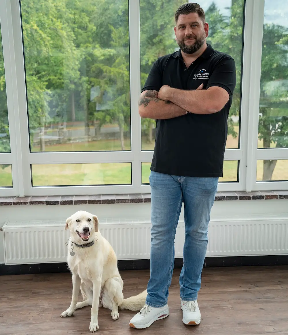 Mitarbeiter von security reasons steht mit verschränkten Armen neben einem hellen Hund